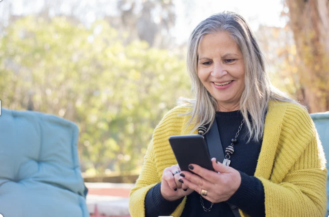 Women sitting on a couch looking down at her cell phone, while using it. 
